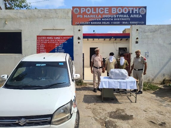 Police personnel, two face-covered men, packages and a car outside a Narela Industrial Area police booth in a Delhi Police photograph.