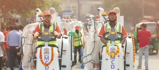 Two MCD sanitation workers operate mechanised litter-picking equipment on a Delhi road