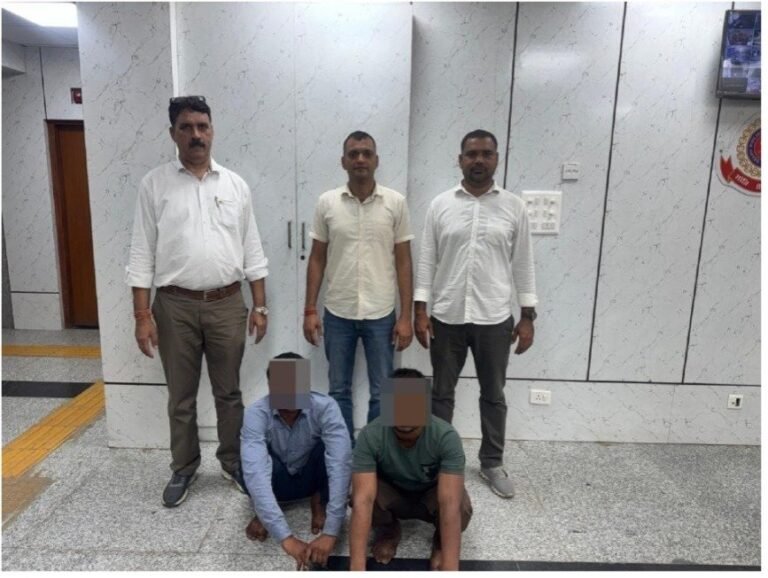 Two face-obscured arrested men seated in front of the police team
