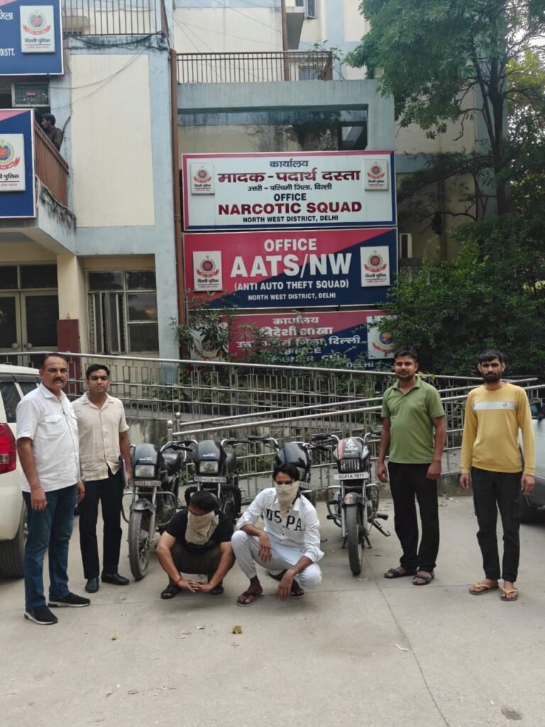 Four motorcycles outside the AATS Northwest Delhi office, with officers and two face-covered men nearby
