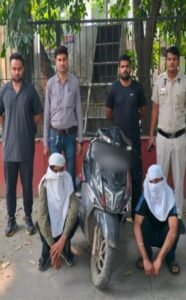 Police photograph showing two seated face-covered accused, a scooty and personnel in Outer Delhi.