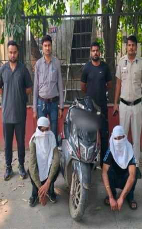 Police photograph showing two seated face-covered accused, a scooty and personnel in Outer Delhi.