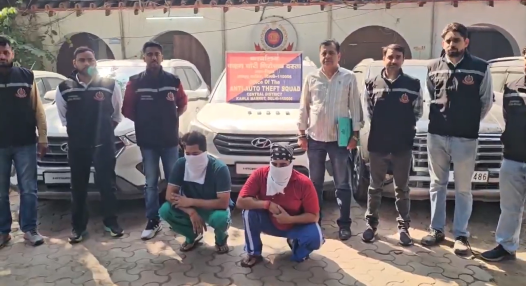 AATS personnel with two seated men whose faces are covered, beside cars outside the Central District office