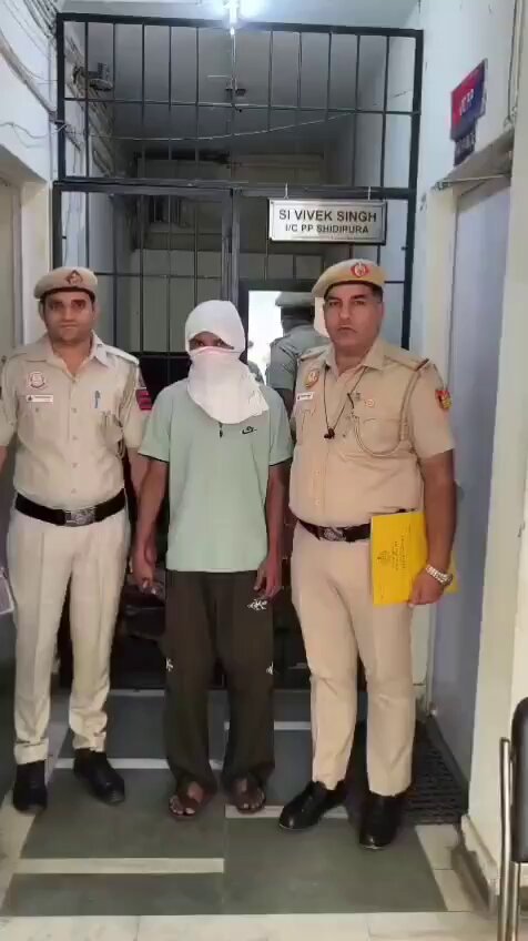 Covered-face person standing between two police personnel outside Sidhpura Police Post