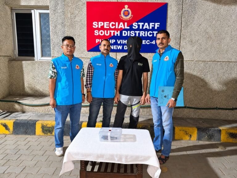 Man wanted in two Mundka cases arrested; pistol and five cartridges recovered Three officers in blue Special Staff vests stand with a hooded man beside a table and a clear case.