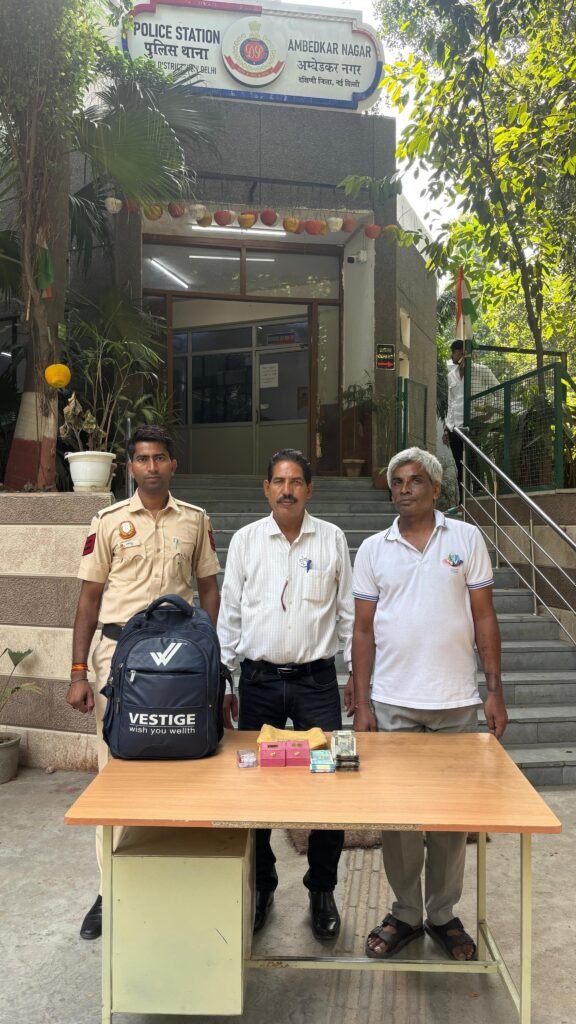 Police officer and two men beside recovered bags, jewellery boxes and cash outside Ambedkar Nagar police station