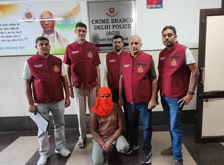 Crime Branch officers stand behind a seated person with his face covered in the official police photograph