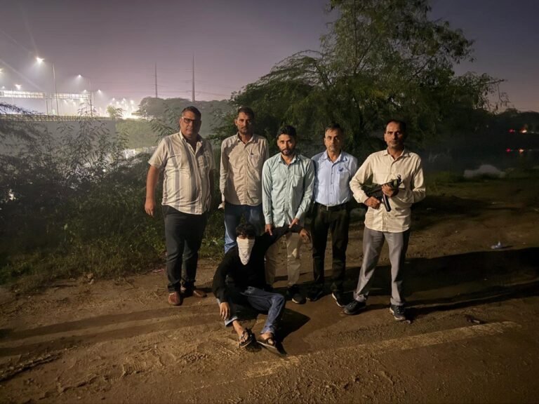 Suspected gang shooter Shivam wounded in Dwarka encounter Five men stand around a crouching man outdoors at night; one standing man holds a long firearm.