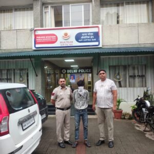 Masked man pictured outside Narela Industrial Area Police Station with two people, one in uniform.